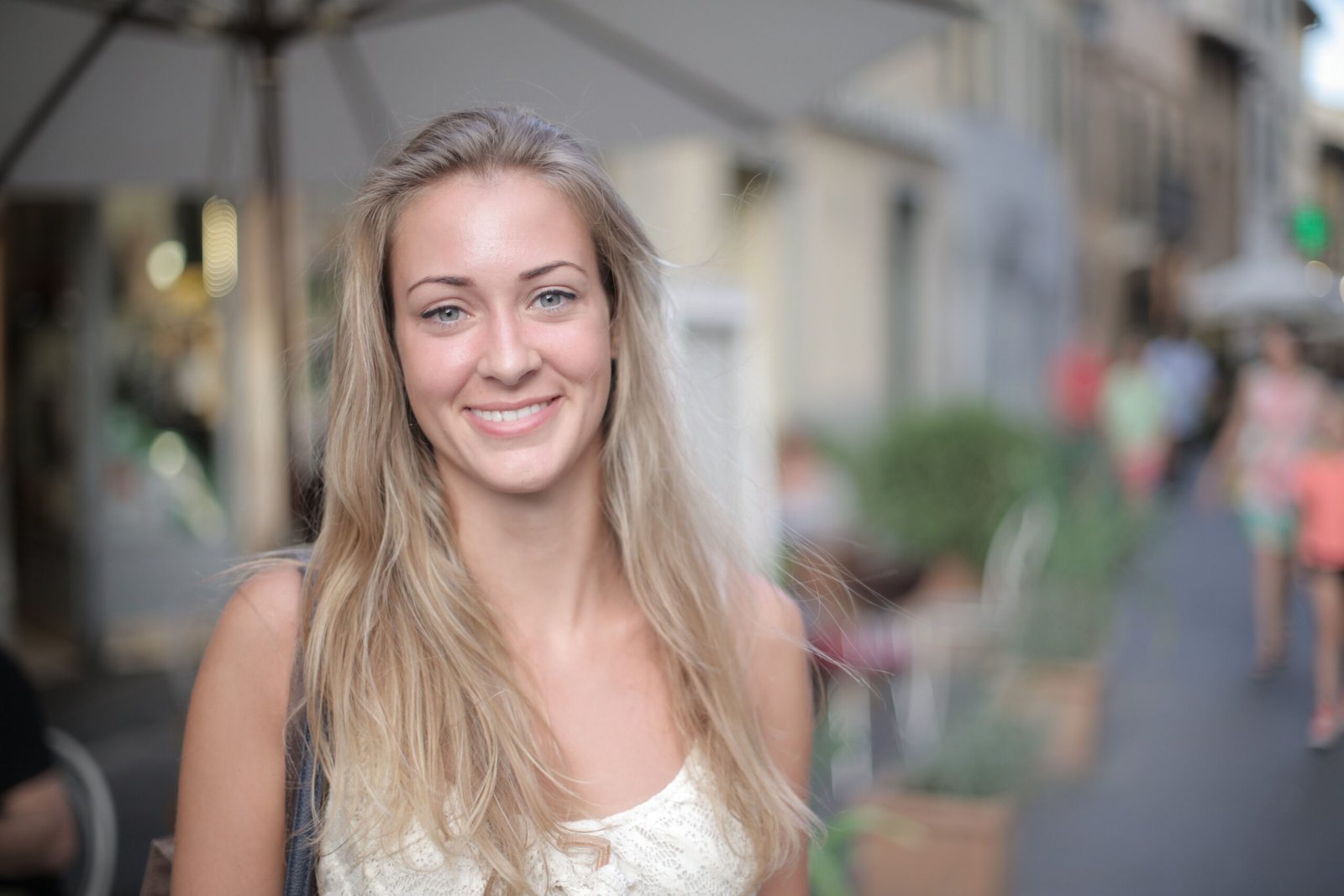 A young woman with blonde hair smiles warmly on a lively city street under daylight.